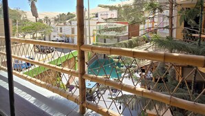 A balcony with a view of a pool area, surrounded by palm trees and buildings. - La casa de Bamboo (Ica)