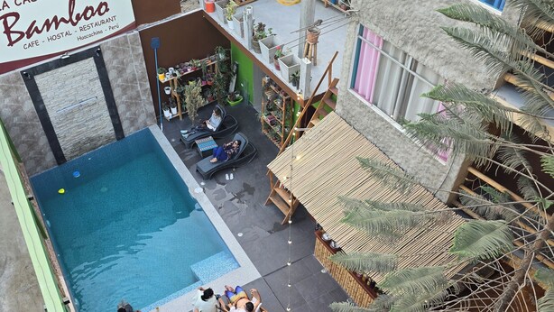 A rooftop pool area with lounge chairs and tables, surrounded by potted plants and a bamboo structure. - La casa de Bamboo (Ica)