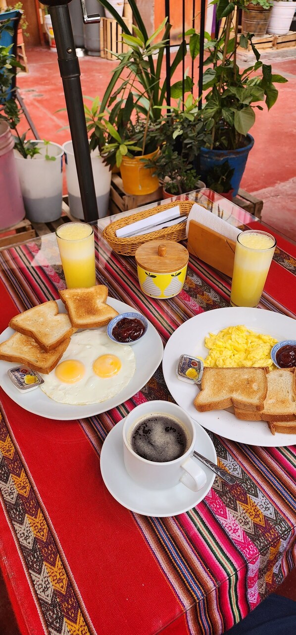 A breakfast setting with two plates of eggs, toast, and beverages on a table with a colorful tablecloth.