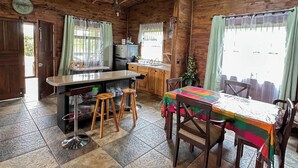 A rustic kitchen with a wooden ceiling, a central island with stools, and a dining table with a colorful tablecloth.