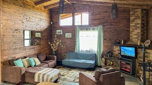 A cozy living room with wooden walls, a fireplace, a television, and a sofa.
