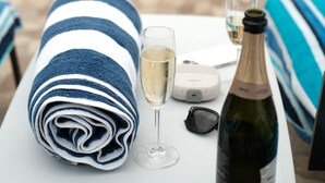 Escena junto a la piscina con una toalla, una copa de champán y una botella de vino sobre una mesa.