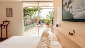 Un dormitorio con una cama grande, una puerta de vidrio que da a un patio al aire libre con una mesa y sillas, y un cuadro en la pared.