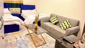 Quarto de hotel com cama, sofá, mesa de centro e pequena mesa com controle remoto.
