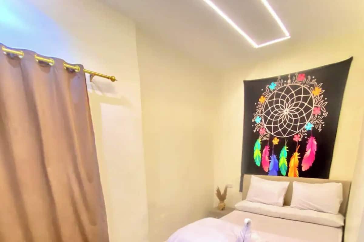A bedroom with a bed, a dreamcatcher, a laptop, and a curtain.