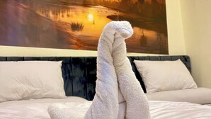 Uma cama com uma toalha em formato de crocodilo, uma pintura do pôr do sol com pirâmides e uma cabeceira de madeira.