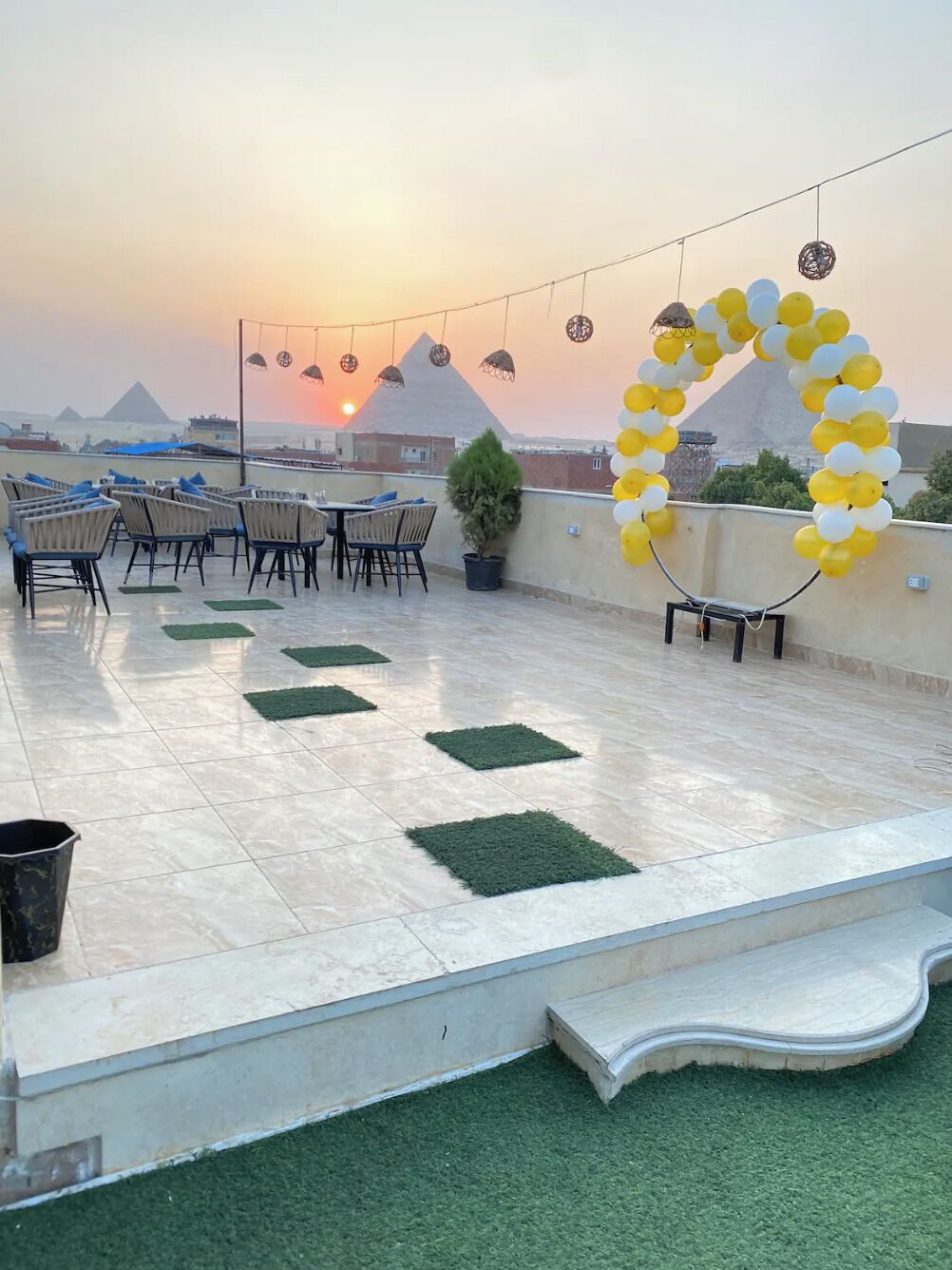 A rooftop terrace with a view of pyramids, arranged seating, and decorative lighting.
