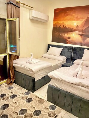 A hotel room with two beds, a large window, an air conditioning unit, and a sunset painting on the wall. - Farsha Pyramids Inn (Giza)