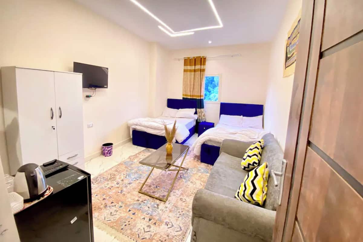 A compact hotel room with a bed, a sofa, a desk, and a wardrobe.