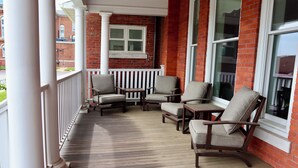 Une véranda en bois avec quatre chaises et une petite table, des balustrades blanches et un mur de briques agrémenté de grandes fenêtres.