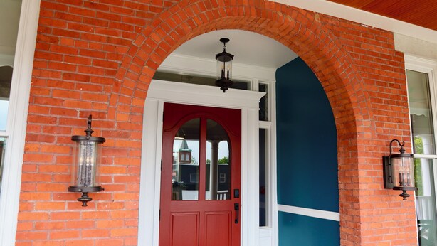 Une porte rouge avec un cadre blanc, une arche en briques et deux lanternes fixées au mur.