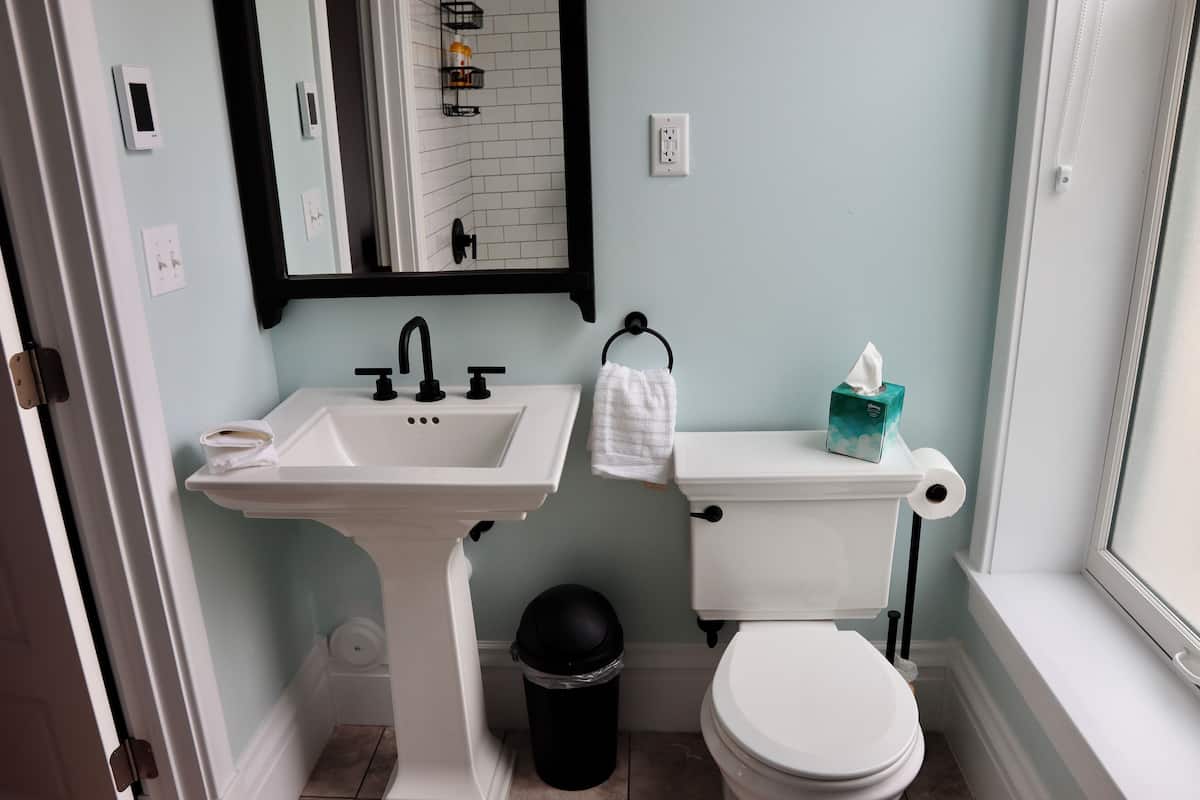 A bathroom with a white sink, black faucet, white toilet, and a black trash bin.