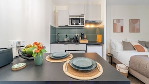 A compact kitchen with modern appliances, a dining area with plates and cutlery, and a bed with a quilted cover.