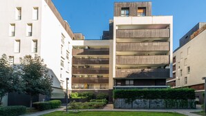 A modern multi-story residential building with balconies, a small rooftop garden, and a well-maintained courtyard with greenery.