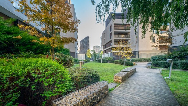 A modern residential area with a wooden pathway, stone planters, and lush greenery.