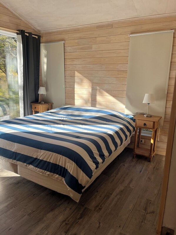 A bedroom with a large bed, wooden walls, two bedside tables with lamps, and a window with curtains.