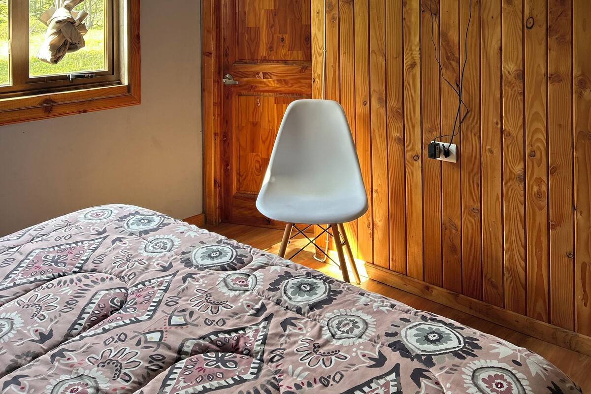 Een slaapkamer met een bed, een aan de muur bevestigde televisie, een raam met gordijnen en een houten deur.