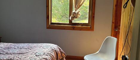 Un dormitorio con cama, una silla, un ventanal con cortinas y paredes de madera.