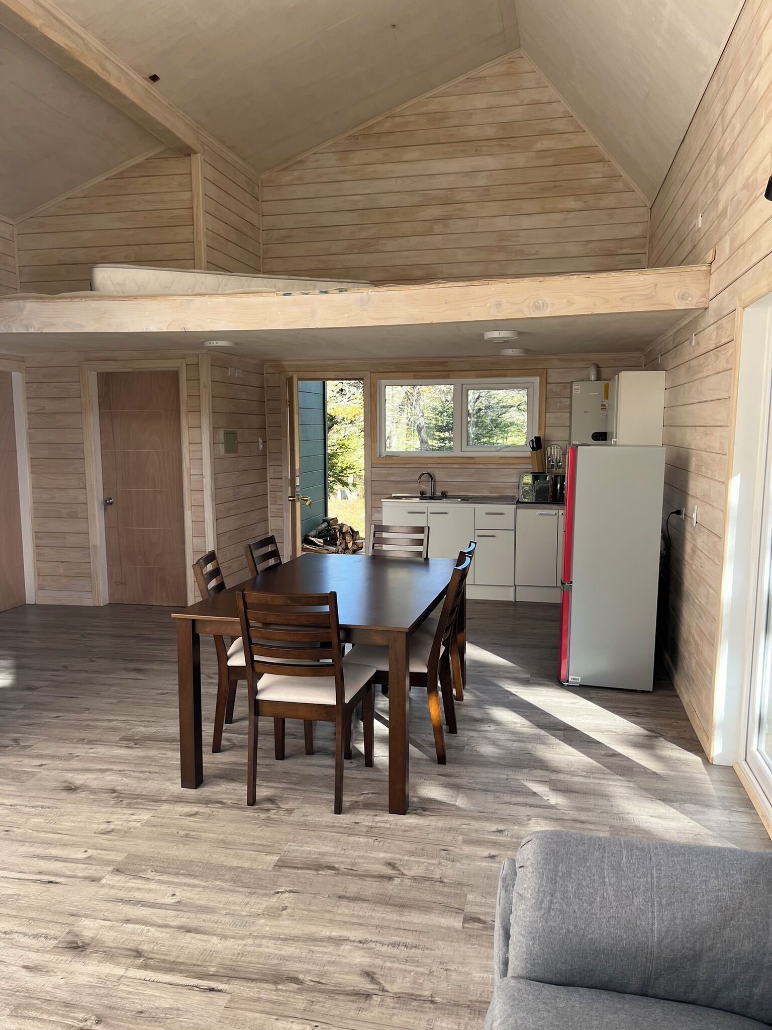 A spacious dining area with a wooden table and chairs, a kitchen with white cabinets and appliances, and a view of the outdoors through a window.
