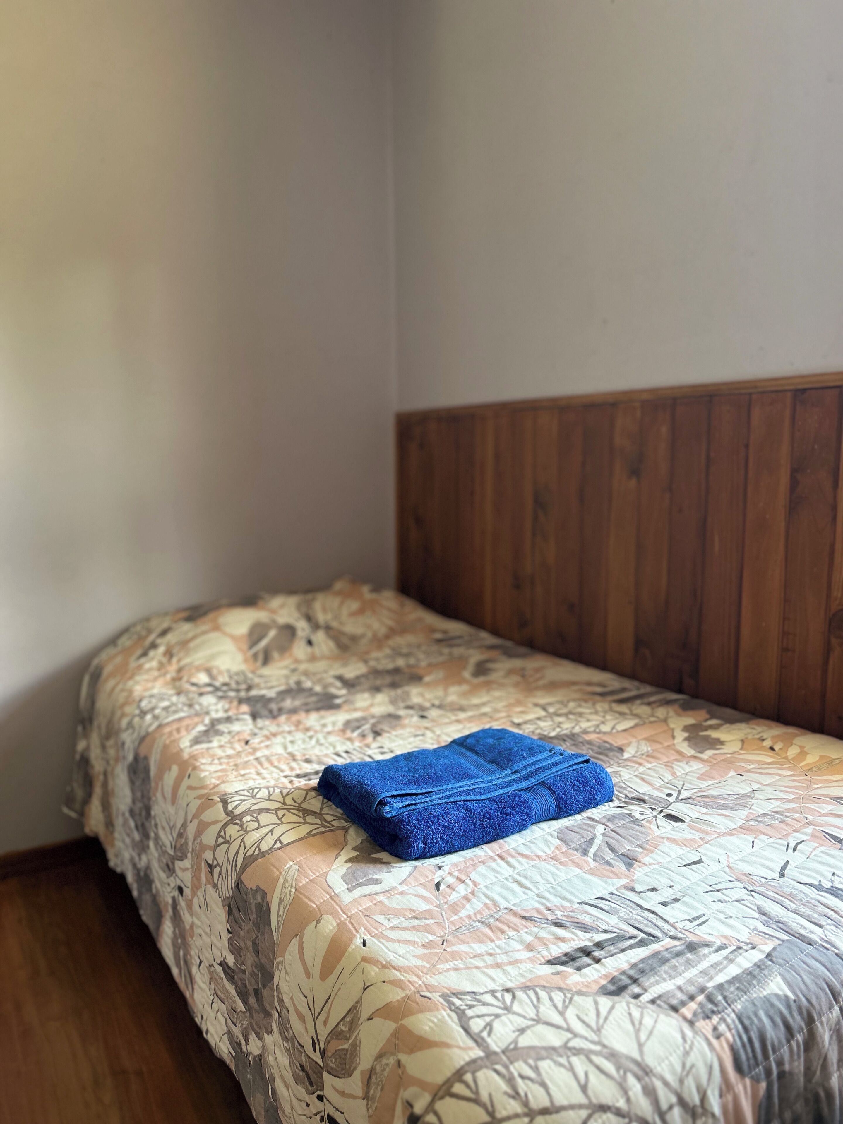 A single bed with a floral-patterned bedspread and a blue towel on it.