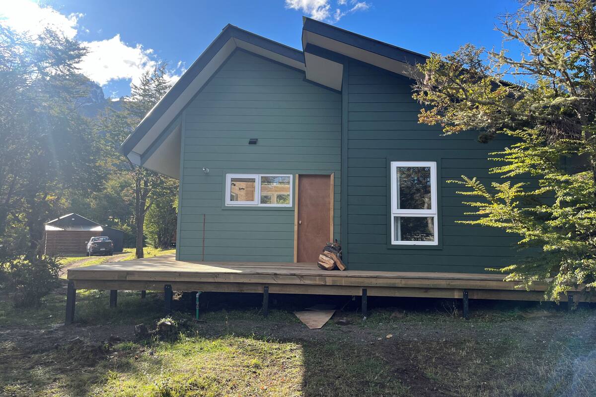 Een groene woning met een veranda, een houten deur en twee ramen.