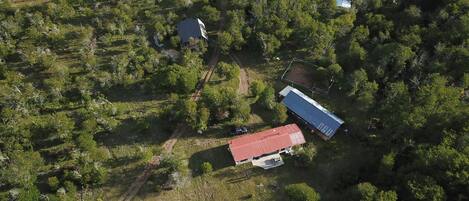 An aerial view of a rural area with a main building featuring a red roof, surrounded by dense greenery and a few smaller structures.