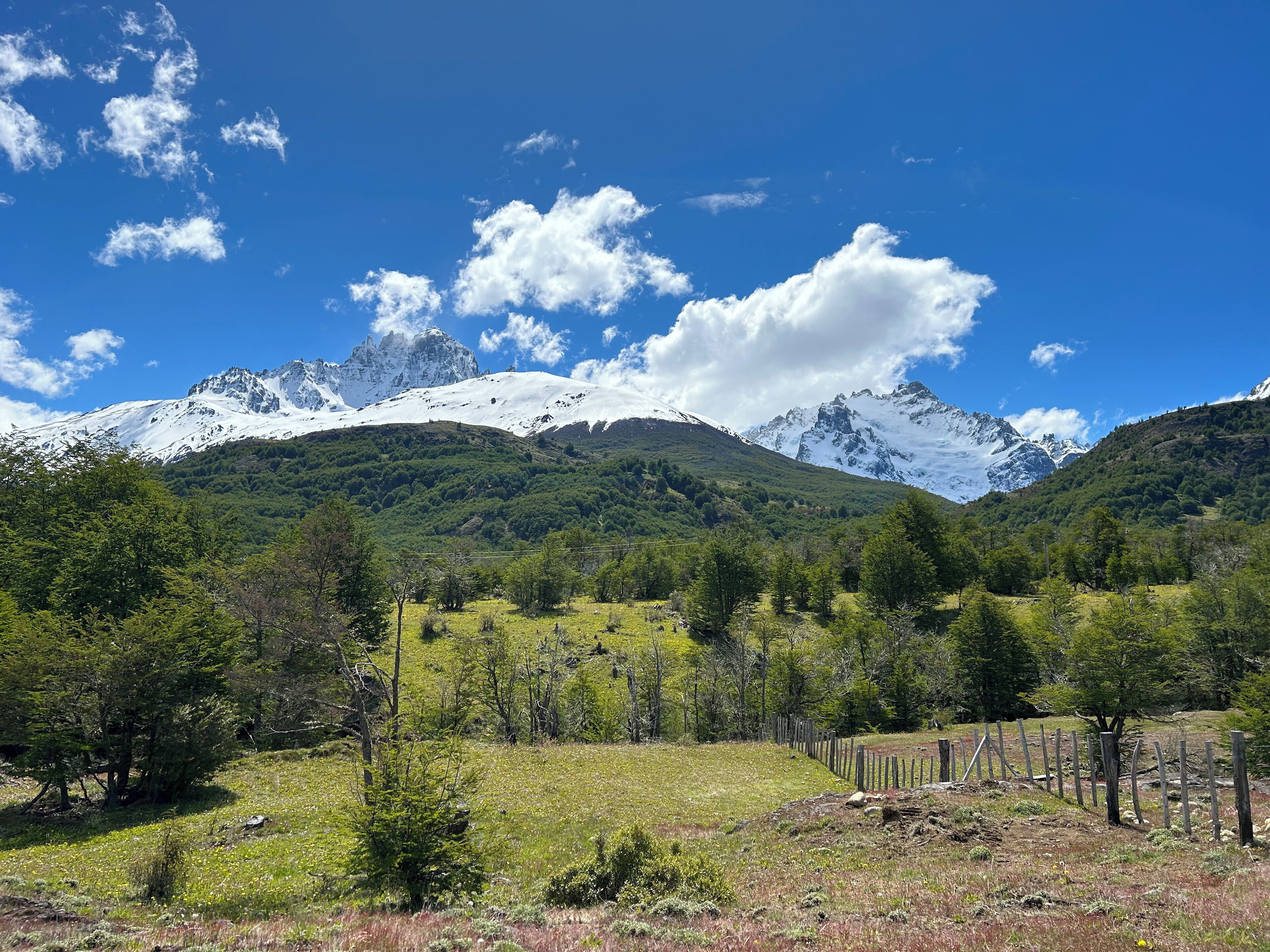 A mountainous landscape with snow-capped peaks, green valleys, and a clear blue sky.