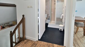 A staircase leading to a bathroom with a shower, toilet, and a small shelf with books.