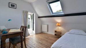 A bedroom with a sloped ceiling, a skylight, a bed, a desk with a chair, a lamp, and a radiator.