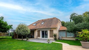 Ein Haus mit einem Ziegeldach, einer Terrasse und einem gepflegten Rasen.