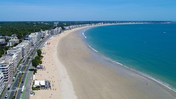 Eine Küstenstadt mit einem breiten Sandstrand, klarem blauem Meer und modernen Gebäuden entlang der Uferlinie.
