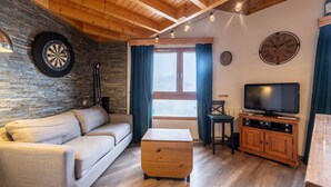 Un salon chaleureux avec un plafond en bois, un jeu de fléchettes, un téléviseur et un canapé.