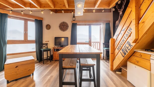 Un intérieur en bois comprenant une table à manger, des bancs, un téléviseur et une vue sur la montagne.