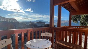 Un balcon en bois avec une table ronde et des chaises, donnant sur un paysage montagneux.