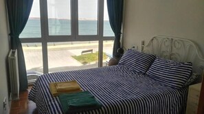 A bed with striped bedding, a view of the sea through large windows, and a metal headboard.