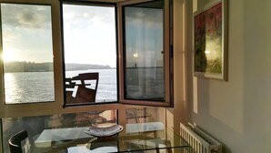 A room with a glass table, a chair, and a view of a body of water through a window. - Seaviews-gijon-parking-2br-walk to Beach-wifi (Gijon)