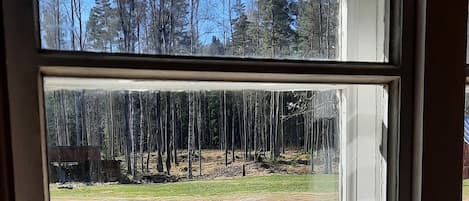 A wooden deck with a table and chairs, a window with a view of a forest and a building in the background.
