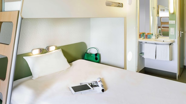 Una cama litera con una mesita de noche, un bolso verde y una tableta sobre la cama.