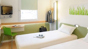 Habitación de hotel con dos camas, un escritorio, una silla, un televisor y una ventana.
