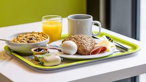 A breakfast tray with cereal, juice, a muffin, a boiled egg, a ham slice, and a small container of jam. - B&B Hotel Berlin Genshagen-nord (Ludwigsfelde)