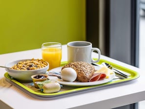 A breakfast tray with cereal, juice, a muffin, a boiled egg, a ham slice, and a small container of jam. - B&B Hotel Berlin Genshagen-nord (Ludwigsfelde)