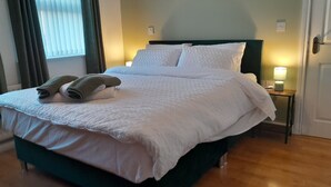 A neatly made bed with white linens and two folded towels, a bedside table with a lamp, and a window with curtains. - Tranquil Retreat Close to the Coast (Coleraine)
