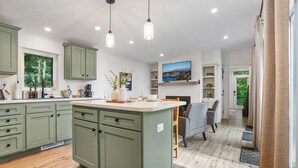 A modern kitchen with green cabinets, a central island, pendant lighting, and a dining area with chairs. - Woodland Chalet  Hot Tub  Fire Pit  Grill (Quarryville)