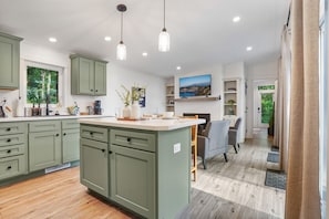 Une cuisine moderne avec des meubles de couleur verte, un îlot central, des luminaires suspendus et un coin repas avec des chaises.