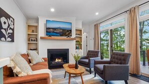 A living room with a fireplace, a sofa, armchairs, a coffee table, and a TV mounted above the fireplace. - Woodland Chalet  Hot Tub  Fire Pit  Grill (Quarryville)