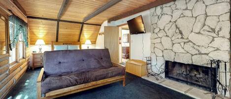 A log cabin interior with a stone fireplace, wooden ceiling beams, and a sofa.