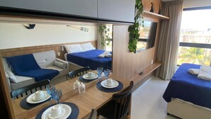 A hotel room with a dining area, two beds, a TV, and a balcony with plants. - Villas do Porto - 312 by La Playa (Ipojuca)