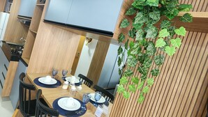 A modern kitchen with wooden cabinetry, a dining area with a table set for two, and a potted plant on the wall. - Villas do Porto - 312 by La Playa (Ipojuca)