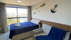 A hotel room with two beds, a sofa, a view of the city, and decorative wall art. - Villas do Porto - 312 by La Playa (Ipojuca)