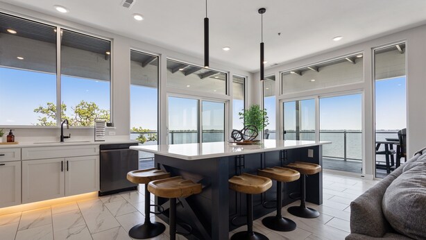 Una cocina moderna con una isla grande, taburetes de bar y ventanas amplias que ofrecen vistas al mar.